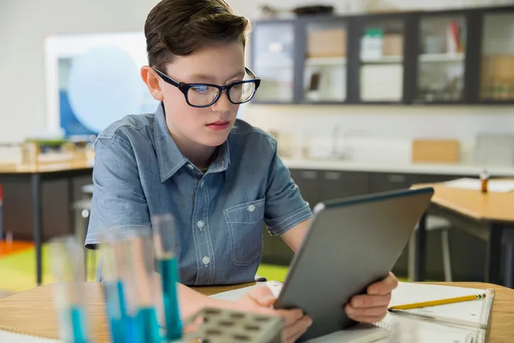 young boy in classroom wearing glasses and looking at a digital tablet